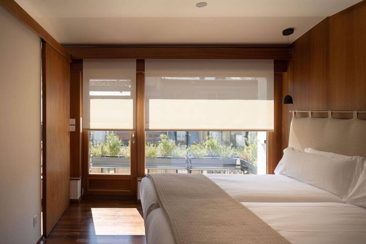 A bedroom with a large bed, a view of greenery outside, and wooden paneling.