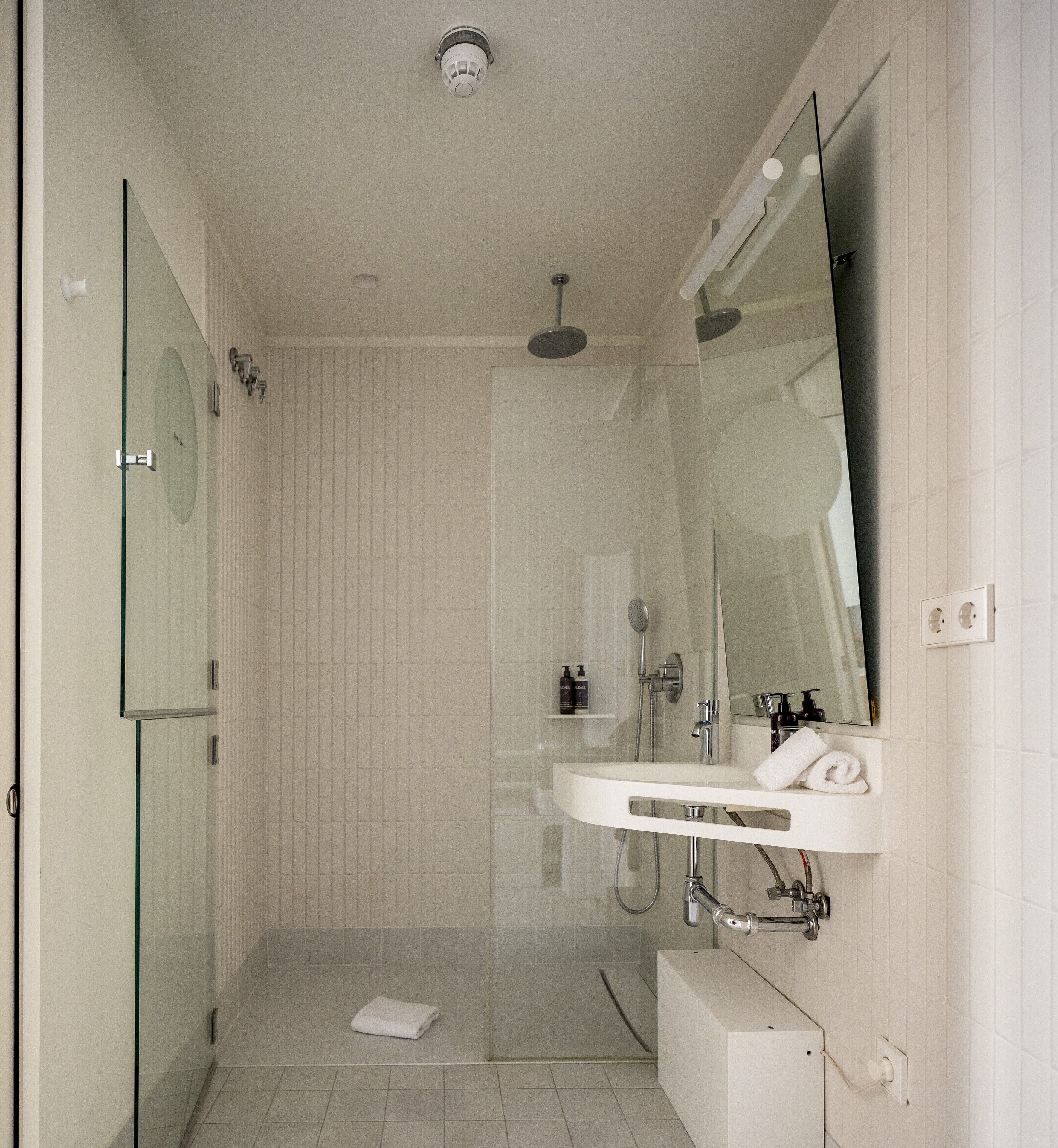 A modern bathroom with a glass shower enclosure, a white sink with a mirror, and a towel on the floor.