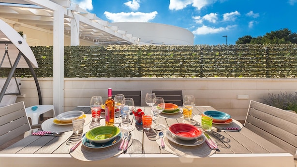 An outdoor dining area with a table set for a meal, surrounded by a white pergola and a view of a vineyard. - 2719 Villino Isidoria by Barbarhouse (Nardò)