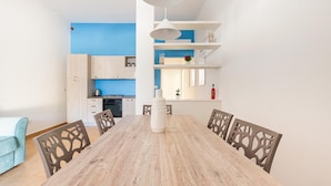 A modern kitchen with white cabinets, a blue wall, and a dining area with a wooden table and chairs. - 2719 Villino Isidoria by Barbarhouse (Nardò)