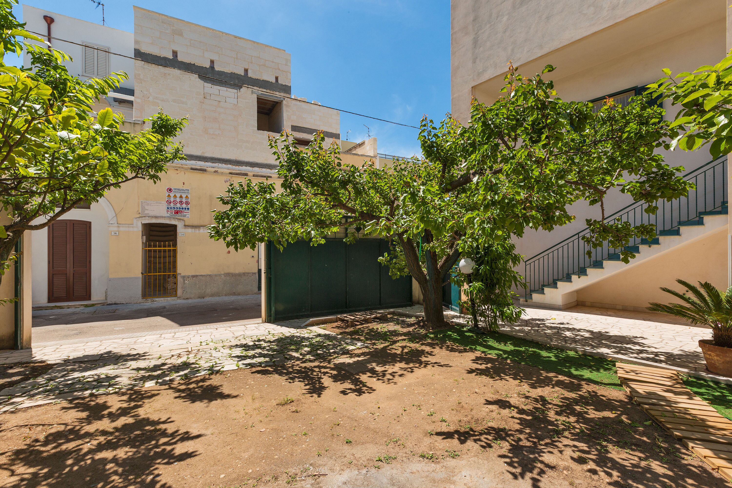 A courtyard with a tree, a green gate, and a staircase leading to an upper level.