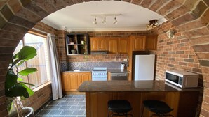 Uma cozinha com arco de tijolos, armários de madeira, uma geladeira branca, um micro-ondas e um vaso com planta.