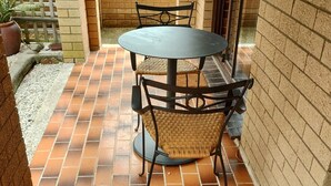 Uma área de pátio com uma mesa redonda e cadeiras, cercada por paredes de tijolo e um chão de azulejos.
