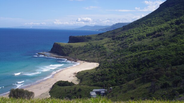 Paisagem costeira com praia, colinas verdes e céu claro.