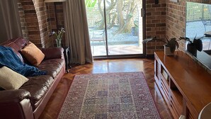 Uma sala de estar com parede de tijolos, sofá de couro, mesa de centro de madeira e tapete estampado.