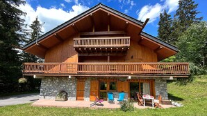 En tvåvånings chalet i trä med en balkong, en grund av sten och en utomhusplats med sittmöbler.