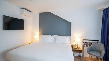Una habitación de hotel moderna con una cama grande, lámparas de noche, un televisor de pantalla plana montado en la pared, un escritorio con una silla y una cortina azul.