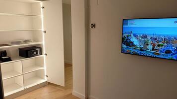 A hotel room with a TV displaying a cityscape, a minibar, and a white wardrobe.