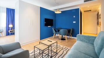 En moderne stue med en blå væg, et fladskærms-tv, et spiseområde med bord og stole samt en sofa.