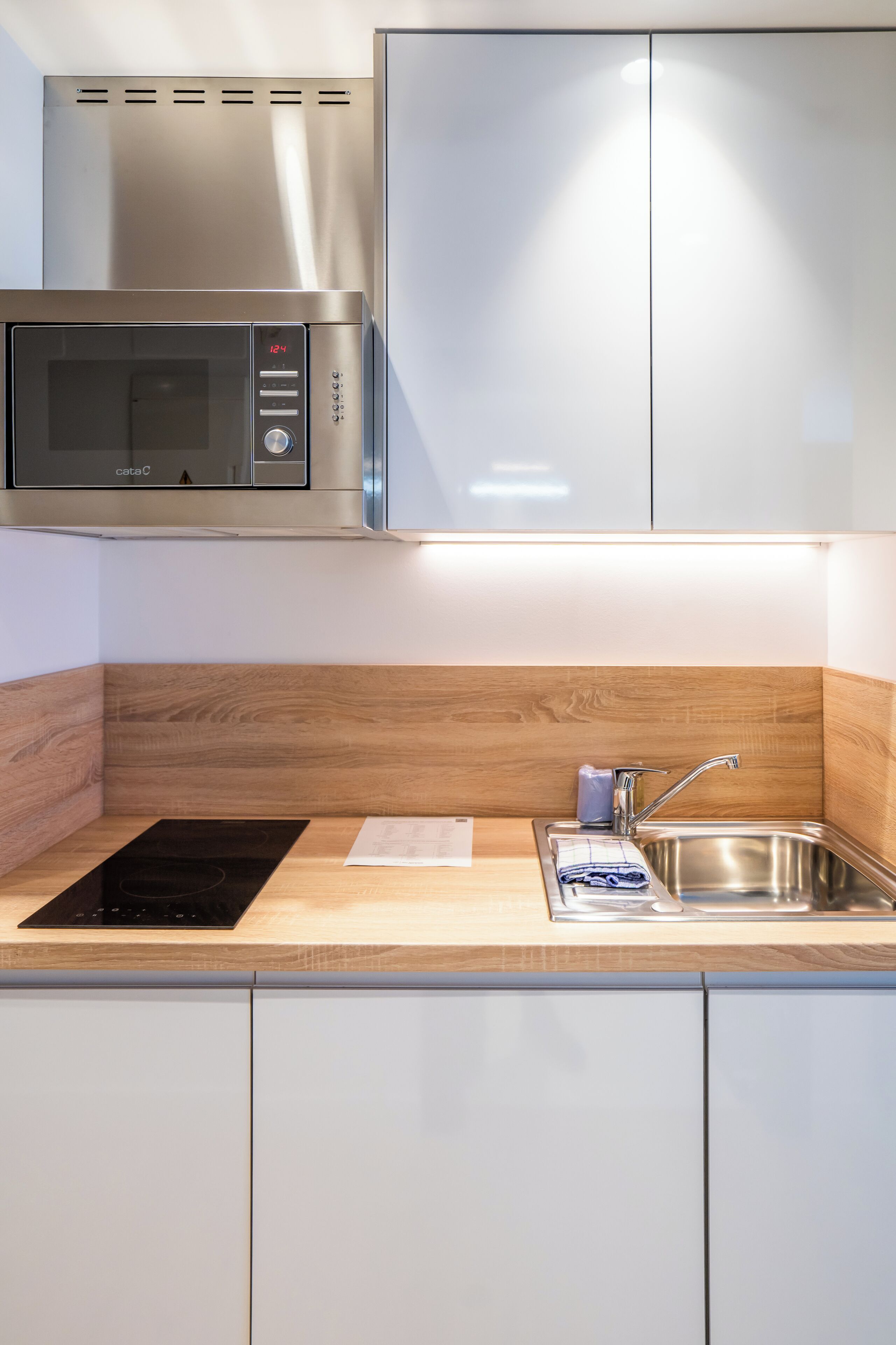Una cocina moderna con microondas integrado, un lavamanos y una encimera de madera.