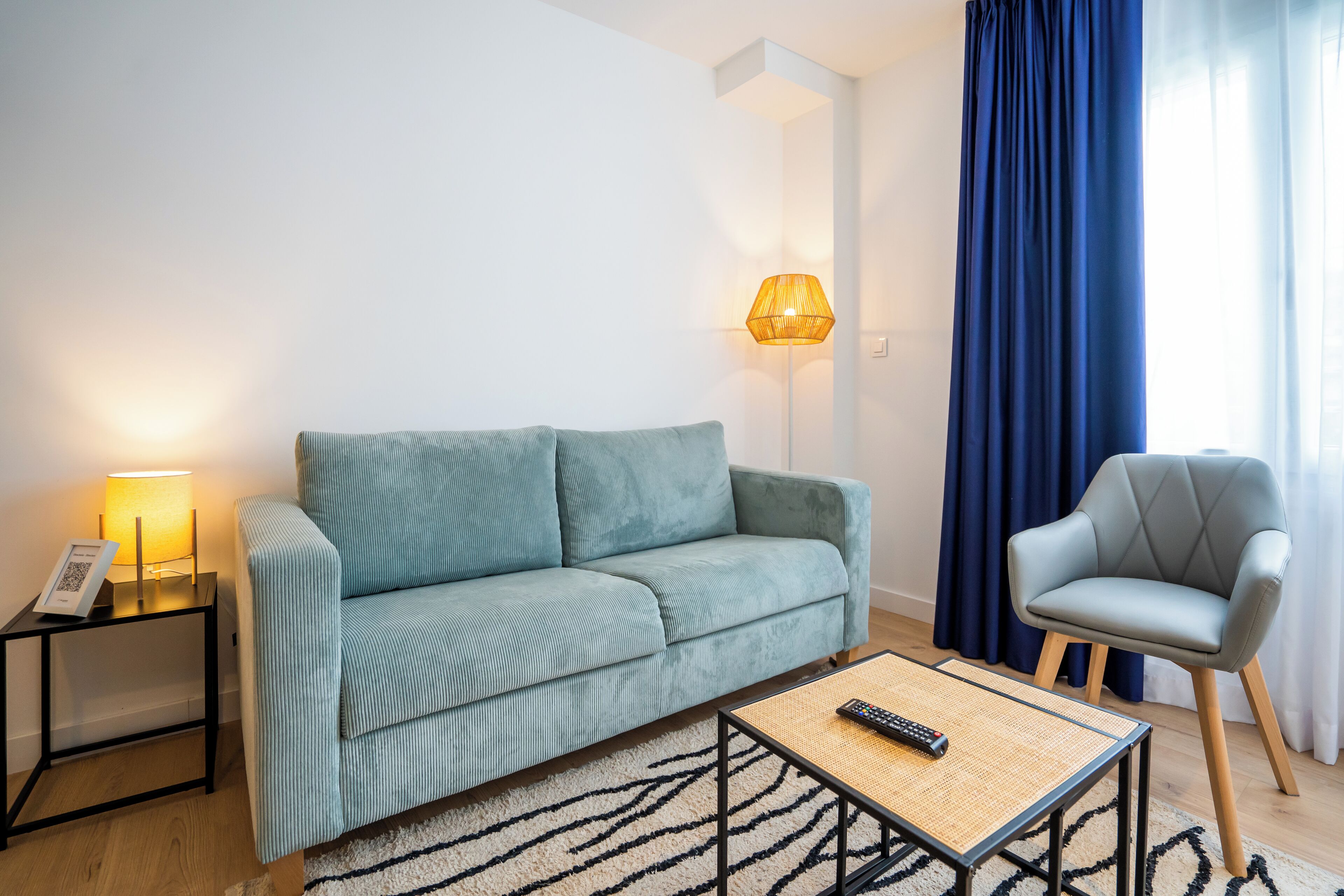 A modern living room with a sofa, a chair, a lamp, and a remote control on a table.