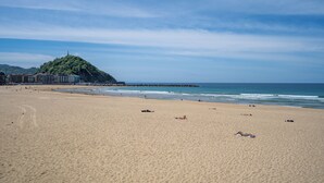 A wide sandy beach with a few people lying on the sand, a rocky outcrop in the distance, and buildings on the left side. - abba Apartments Playa de Gros San Sebastián (San Sebastián)