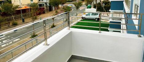 A balcony with a metal railing overlooking a road with cars and buildings.