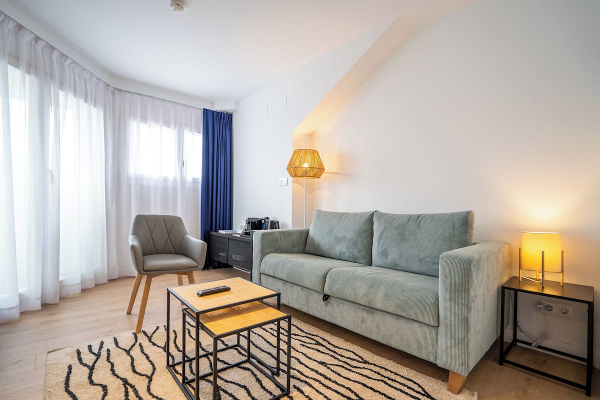 Een moderne woonkamer met een bank, fauteuil, salontafel, lamp en vloerkleed.