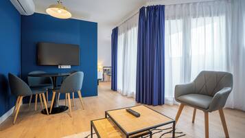 Un salon moderne doté d’un téléviseur à écran plat, d’une table à manger avec des chaises, d’un canapé et d’une grande fenêtre agrémentée de rideaux.