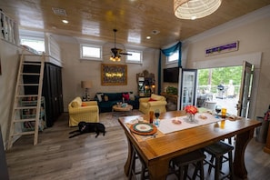 A spacious living area with a wooden ceiling, a dining table set for two, a sofa, a dog, and a ladder against the wall. - Side-By-Side Both Places, Groups Can Spend More Time Together! (New Iberia)