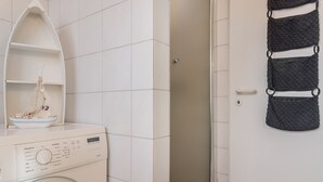A washing machine with a control panel, a shelf with a decorative item, and a towel rack with towels. - Das Ferienhaus "lennox" mit 70 qm Wohnfläche Bietet Ausreichend Platz für bis zu (Carolinensiel)