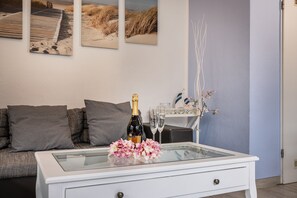 Una sala de estar moderna con una mesa de centro de vidrio, una botella de champán y un jarrón con flores.