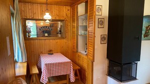 Una habitación acogedora con paredes de madera, una mesa a cuadros, un banco, una chimenea y una ventana con vistas.
