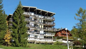 Un edificio de varios pisos con balcones, rodeado de árboles y vegetación.