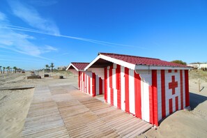 A beachside building with a red and white striped exterior, a wooden deck, and a clear blue sky.