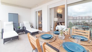 A dining area with a wooden table set for four, surrounded by wicker chairs, and a view of the city through large windows.