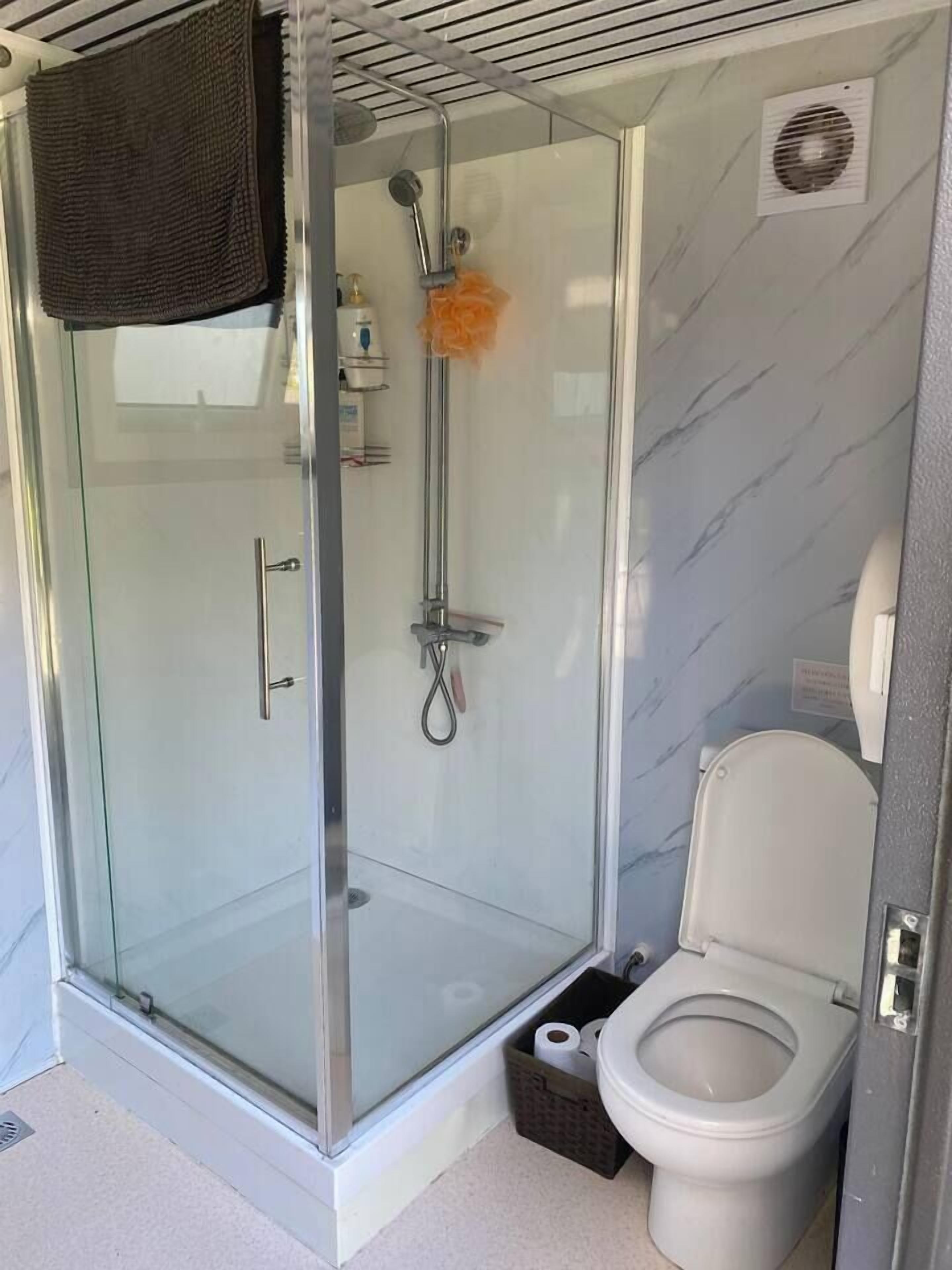 A modern bathroom with a glass-enclosed shower, a toilet, and a small storage basket.