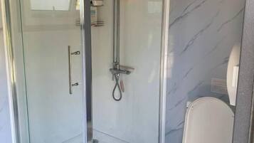 A modern bathroom with a glass-enclosed shower, a toilet, and a small storage basket.