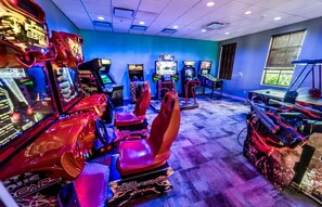 Una sala de juegos recreativos con varias máquinas de carreras y un gran modelo de coche de carreras rojo.