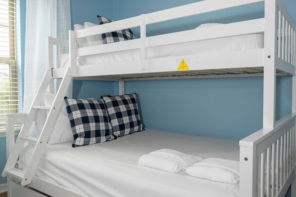 A bunk bed with a safety warning sign, white bedding, and a checkered pillow.