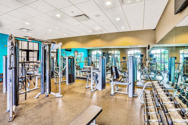 Un gimnasio con diferentes máquinas de ejercicio, una banca y mancuernas.