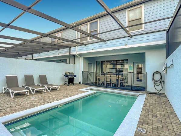 A pool area with lounge chairs, a grill, and a covered seating area.
