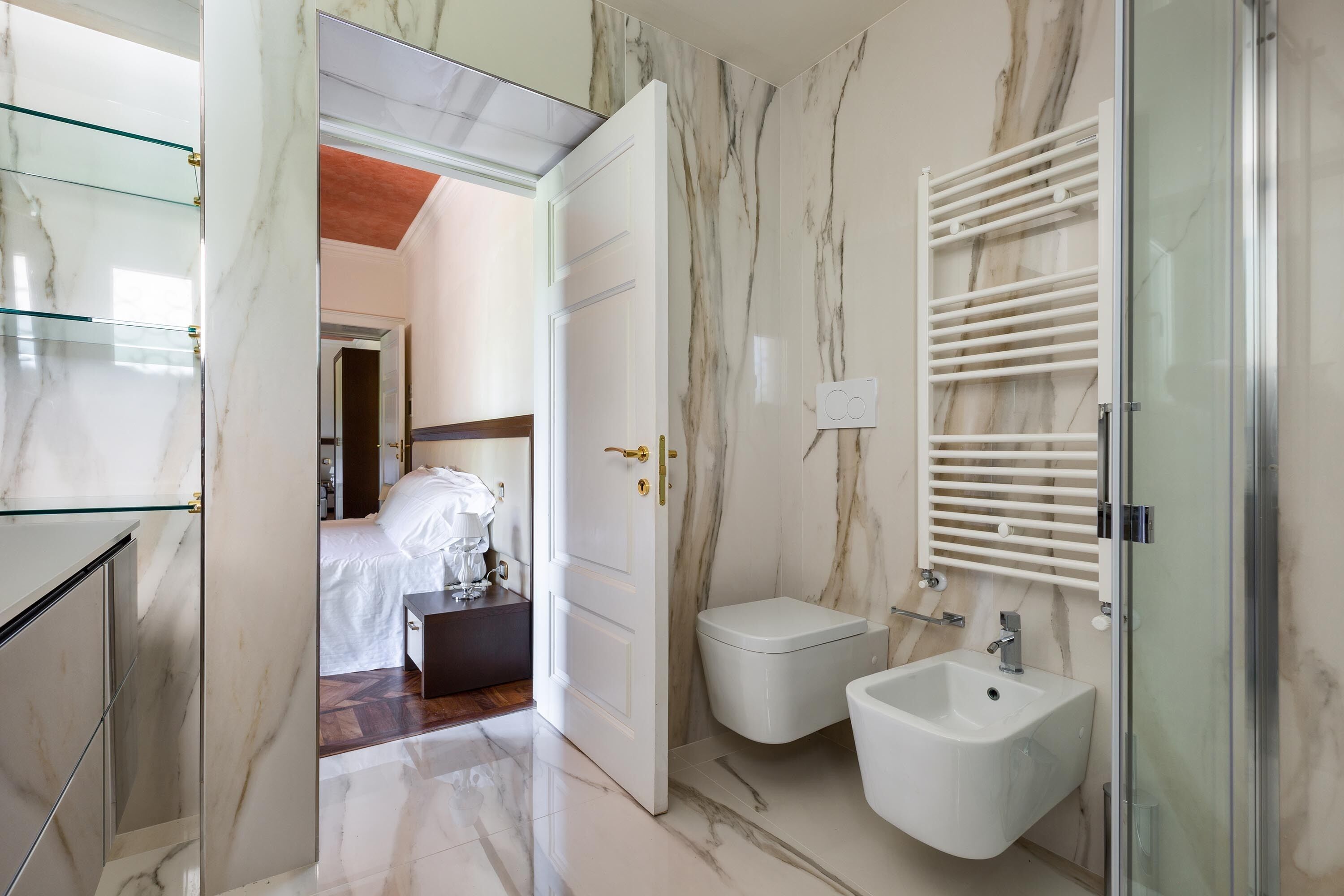 Un bagno moderno con pavimento in marmo, un bidet, box doccia in vetro e porta doccia in vetro.