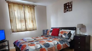 A bedroom with a bed, a nightstand, a lamp, a TV, and a window with curtains. - Lovely 2-bed Apartment in Aberdeen (Aberdeen)