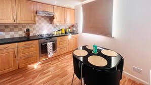 A compact kitchen with wooden cabinets, a black countertop, and a small table with four beige placemats. - Lovely 2-bed Apartment in Aberdeen (Aberdeen)