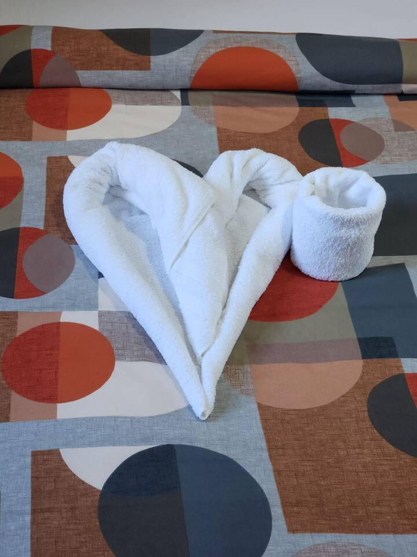 A white towel folded into a heart shape on a patterned fabric.