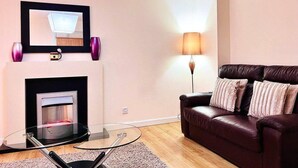 A modern living room with a glass coffee table, a leather sofa, a fireplace, and a wall-mounted mirror. - Lovely 2-bed Apartment in Aberdeen (Aberdeen)