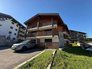 A multi-story residential building with balconies, a car parked in front, and a well-maintained lawn.