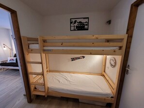 Una cama individual con estructura de madera, colchón blanco y una pequeña repisa. Hay un cartel en la pared con texto e imagen.