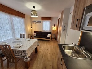 A compact kitchen with a dining area, wooden cabinets, a stainless steel sink, and a table set for four.
