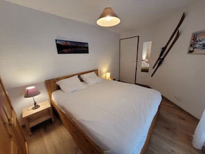 A bedroom with a wooden bed, a nightstand with a lamp, a painting on the wall, and a mirror.