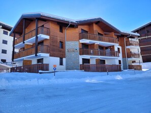 A multi-story hotel with balconies, a sign indicating a ski resort, and a snow-covered ground.