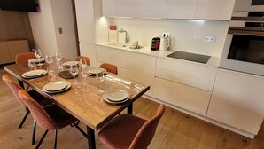 Una cocina moderna con armarios blancos, horno empotrado y zona de comedor con mesa de madera y sillas naranjas.
