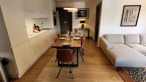 Una cocina moderna con armarios blancos, una mesa de comedor preparada para cuatro personas y un sofá en la sala.