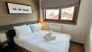 Un dormitorio con cabecera de madera, cama con ropa de cama blanca, un cuadro enmarcado de bisontes en la pared y una ventana con vistas a casas.