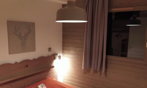 A room with a wooden headboard, a wall-mounted deer head artwork, a hanging light fixture, and a window with curtains.
