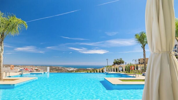 Une piscine d’un bleu éclatant, dotée de chaises longues et de parasols, qui offre une vue imprenable sur le paysage côtier.