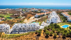 Un quartier résidentiel en bord de mer, avec des immeubles modernes aux façades blanches, une piscine et une vue sur la mer.