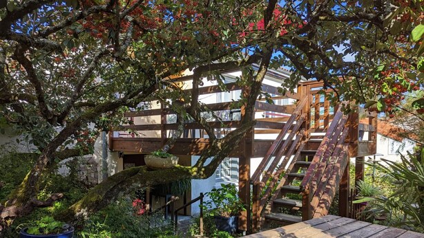 A wooden deck with a picnic table, surrounded by lush greenery and a tree with red berries. - Charming apartment with terrace and garden, perfect for 4 people, in Barbezieux (Barbezieux-Saint-Hilaire)