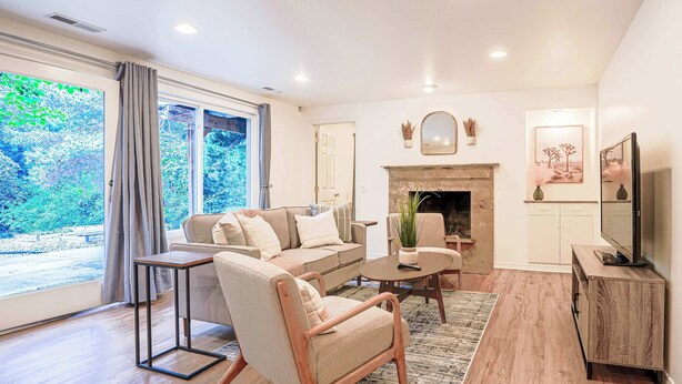 A living room with a sofa, armchair, coffee table, TV stand, fireplace, and large windows. - Serene Mercer Island 3B Lower Unit near LR station (Mercer Island)